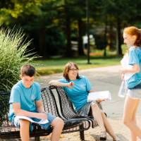 A teacher smiles while speaking with two campers outside.